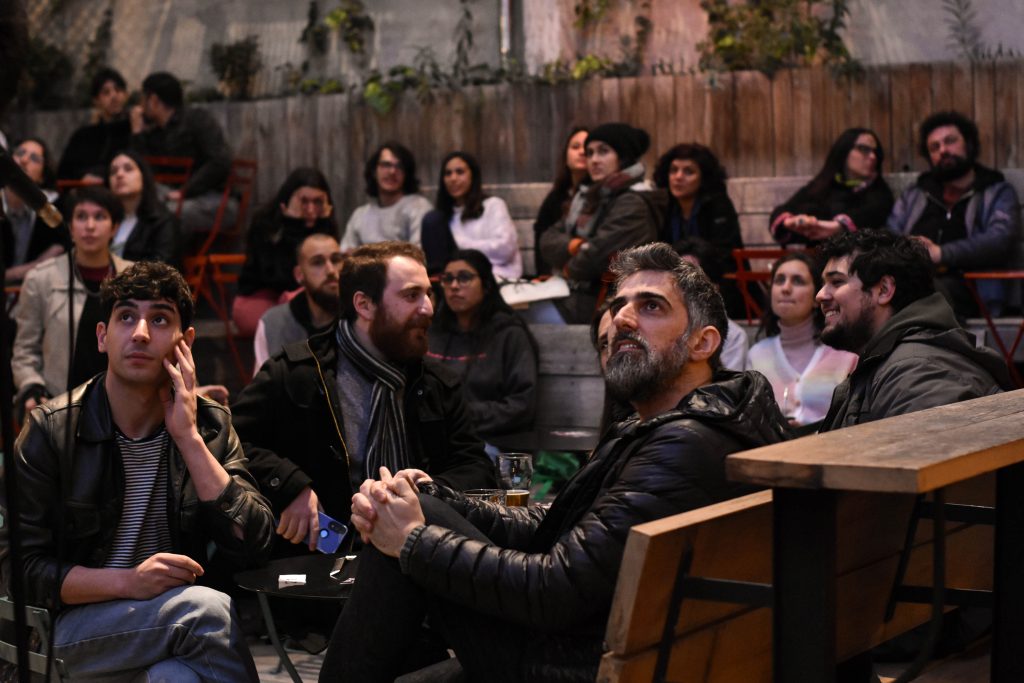 un grupo de personas sentadas en un patio de comidas miran hacia arriba, fuera de pantalla